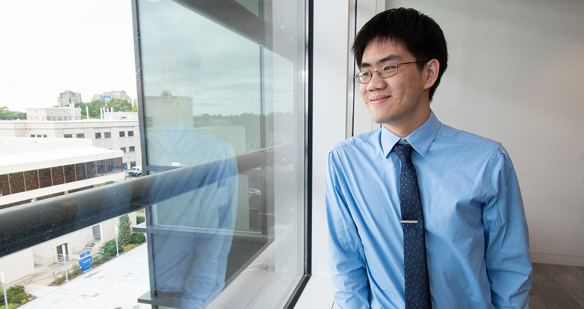 Male student wearing tie looking out window, smiling