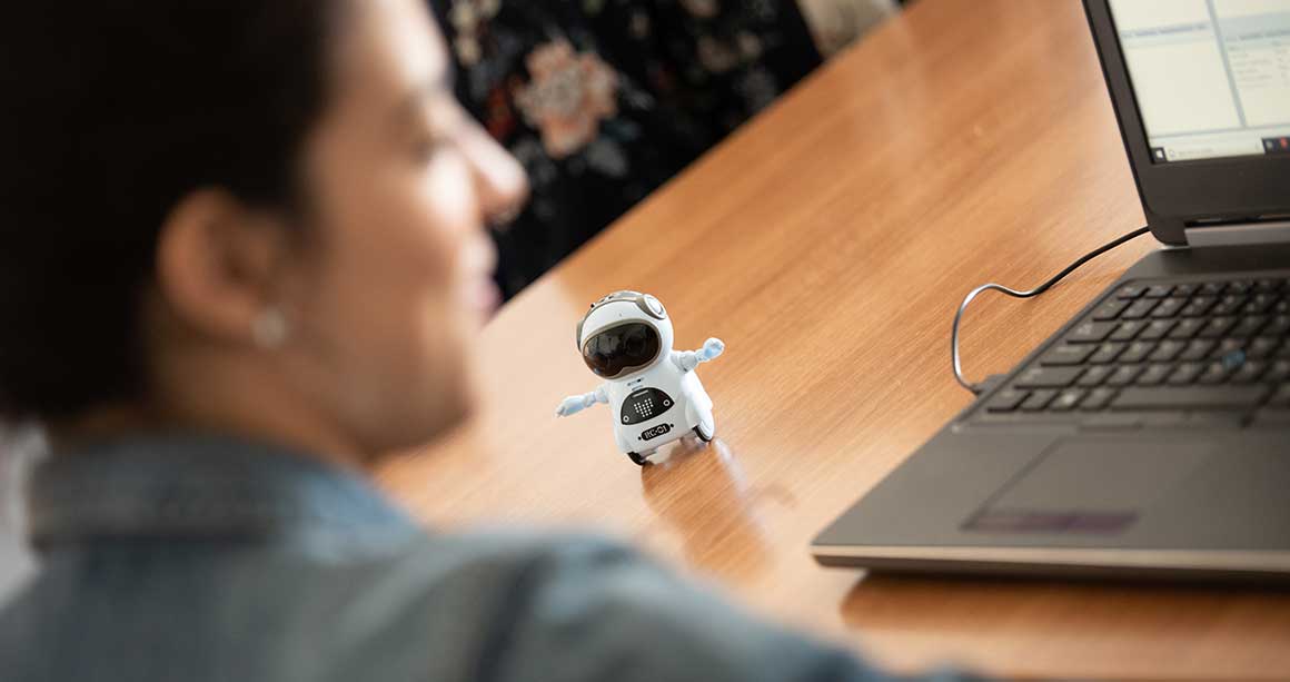 Woman sitting at computer with small robot on table