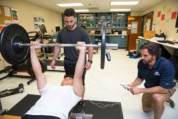 Professor advising students on lifting weights