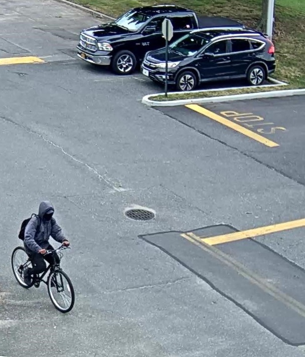 A male was wearing a grey windbreaker and dark denim pants riding on bike