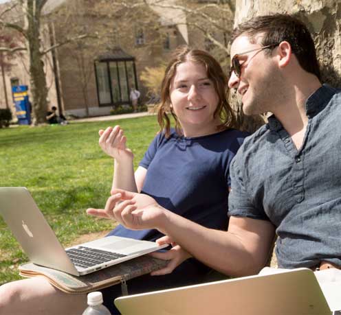 Two students smiling while using a laptop