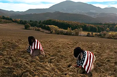 2 Native Americans in a field wrapped in American flag
