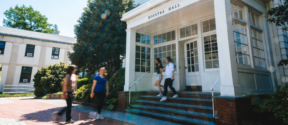 Front view of Hofstra Hall at Hofstra University, with four people walking near the entrance steps