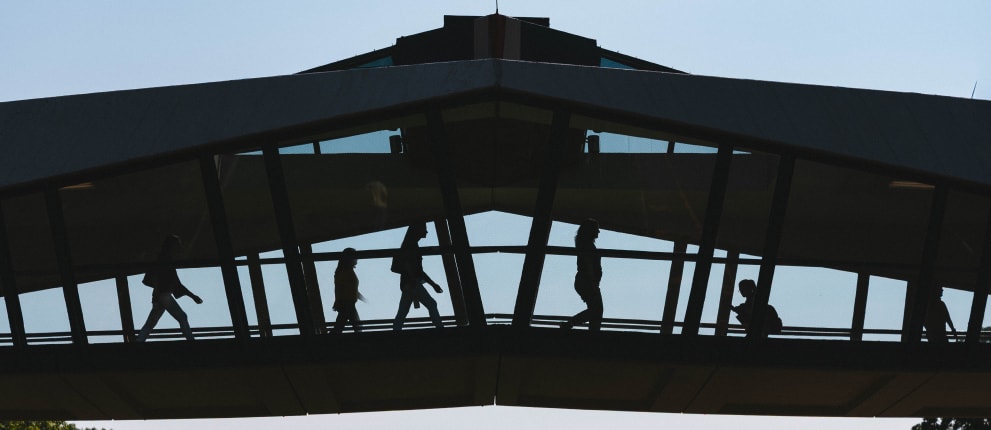 Silhouettes of people walking across the iconic unispan bridge, with sunlight highlighting their outlines against the bright sky.