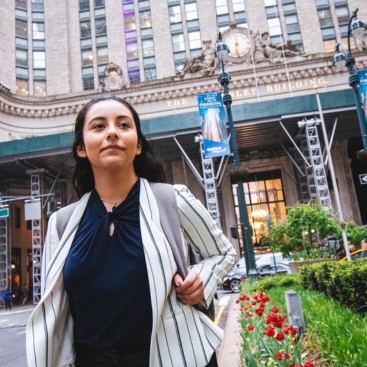 A woman with a backpack walks confidently on a city street in front of The Berkeley Building, with flowers and scaffolding visible.