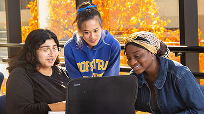 3 students smiling and looking at a laptop